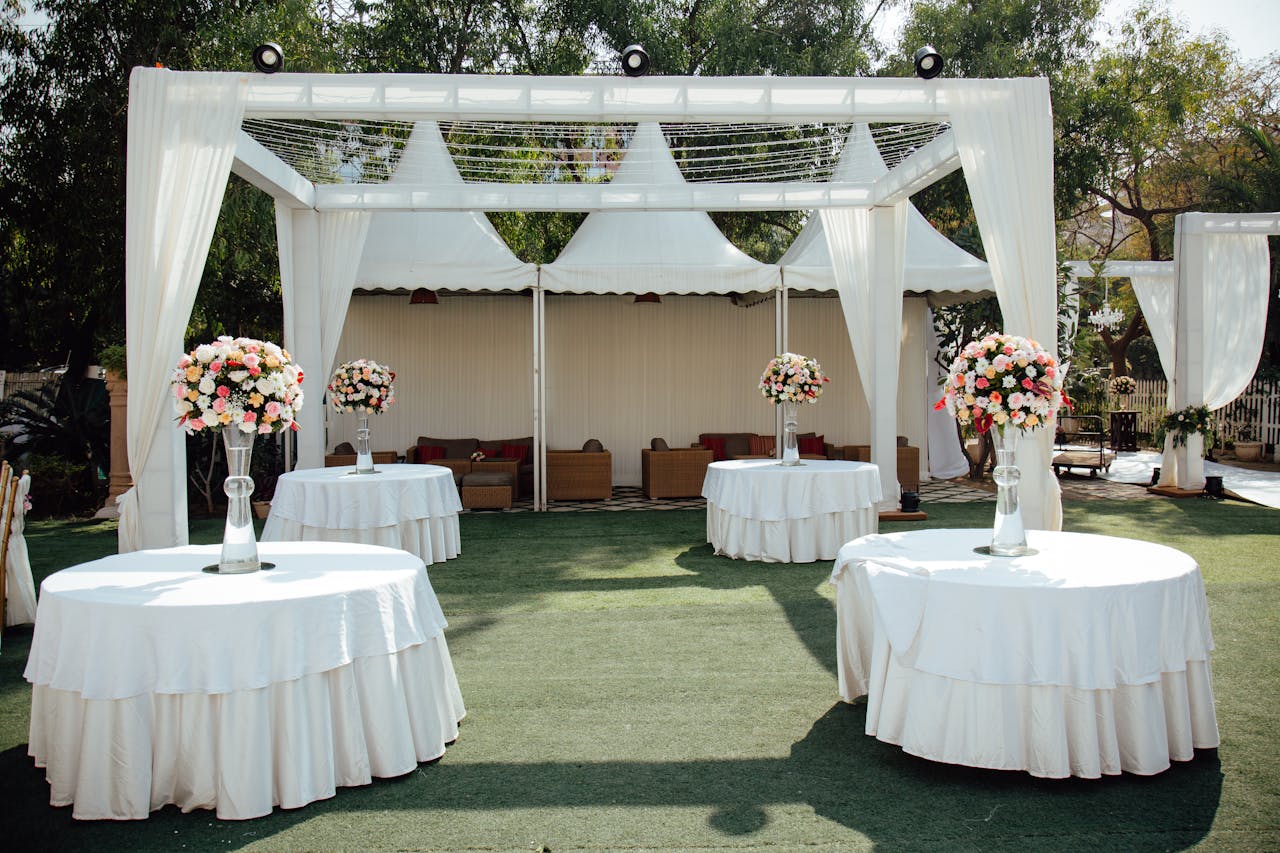 Home Charming outdoor wedding setup with white draped pergolas and floral centerpieces under a sunny sky.